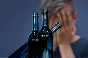 Man with hands covering face behind empty bottles