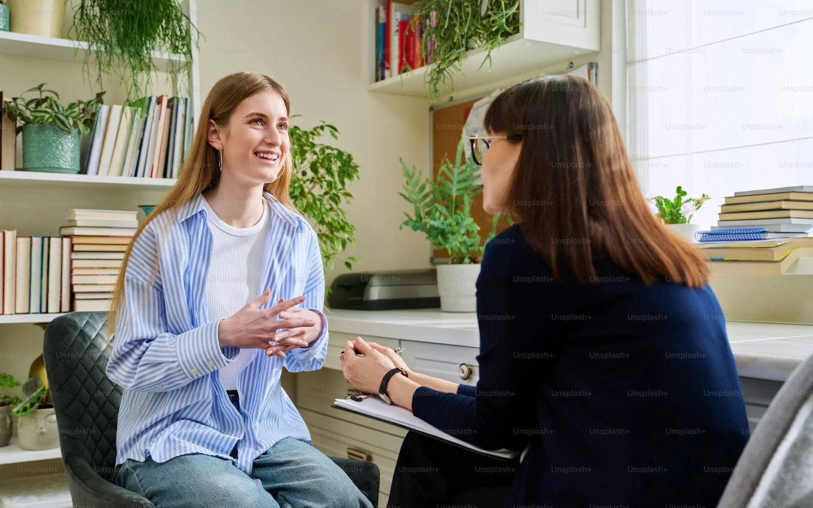 Smiling positive young teen female patient talking to professional mental therapist. Teenager girl high school college student in therapy with psychologist psychotherapist counselor. Treatment support